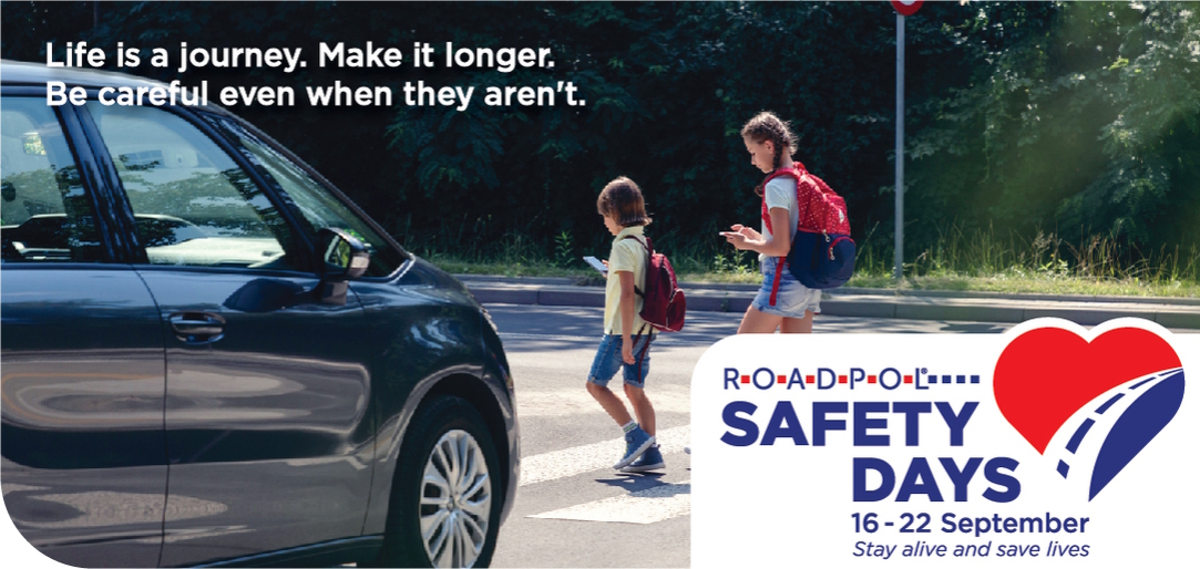 Plakat promujący działania ROADPOL Safety Days. Na plakacie widzimy dwoje dzieci zapatrzonych w telefony komórkowe i przechodzących przez przejście dla pieszych. Przed przejściem stoi samochód. W lewej górnej części plakatu tekst "Życie to przygoda. Spraw by trwała dłużej. Uważaj nawet jeśli oni nie uważają." W prawym dolnym rogu logo ROADPOL Safety Days. 