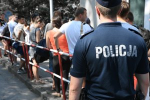 policjant odwrócony plecami, na koszulce napis POLICJA, w tle grupa osób