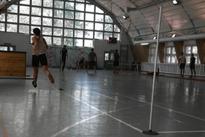 osoby ćwiczą na hali sportowej,  po lewej stronie biegnie kobieta, w tle ćwiczą inne osoby