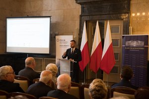 Zdjęcie kolorowe. Przedstawia uczestników konferencji oraz prowadzącego dyrektora Wydziału Rodziny i Polityki Społecznej Śląskiego urzędu Wojewódzkiego  Marcina Chroszcza