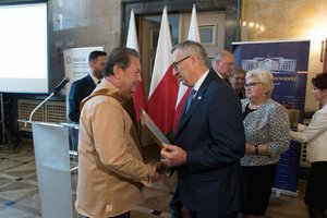 Zdjęcie kolorowe. Zdjęcie przedstawia wręczenie wyróżnienia Najaktywniejszy Senior Panu Markowi Judyckiemu przez Sekretarza Stanu