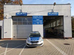 Na zdjęciu policyjny radiowóz stojący przed wjazdem do stacji diagnostycznej.