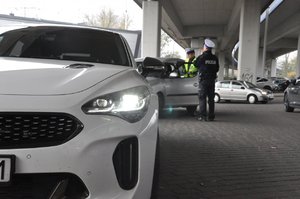 zdjęcie kolorowe: policjanci z grupy speed podczas wykonywania czynności na  drodze. Widok z niskiej perspektywy na  pierwszym planie nieoznakowany radiowóz.