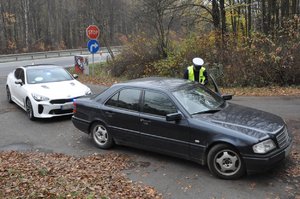 zdjęcie kolorowe: policjanci z grupy speed podczas wykonywania czynności na  drodze. Nieoznakowany radiowóz stoi za  samochodem marki mercedes. Policjant sprawdza  dokumenty kierującego.