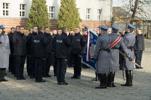 Zdjęcie kolorowe, przedstawiające policjantów z pocztem sztandarowym wraz z nowo przyjętymi funkcjonariuszami.