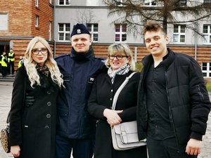 Policjant pozuje do zdjęcia razem z rodziną. W tle budynek koszarów policyjnych.