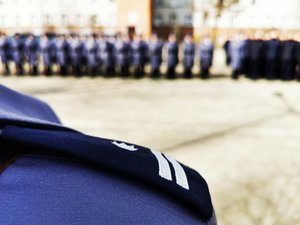 Zbliżenie na pagon z prawego ramienia policjanta. W tle policjanci w szyku.