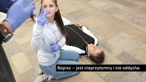 na zdjęciu nastolatka, która udziela pomocy nieprzytomnemu chłopakowi oraz jej kolega, który powiadamia o zdarzeniu służby