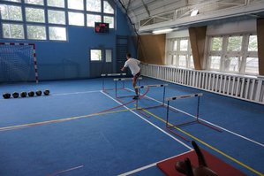 Mężczyzna pokonuje jeden z fragmentów toru przeszkód - pokonanie górą płotków lekkoatletycznych.