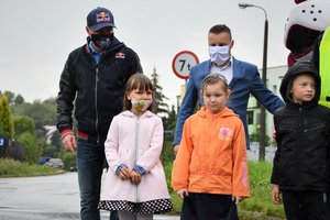Zdjęcie kolorowe. Policjanci i Adam Małysz przeprowadzają dzieci przez ulicę