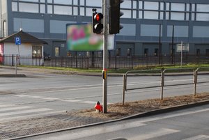 Zdjęcie kolorowe. Teren przejścia dla pieszych. Widoczny czerowny znicz.