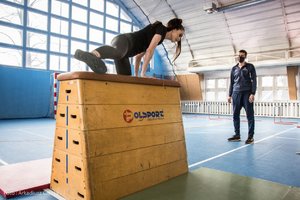Zdjęcie kolorowe. Widoczna Miss Polski 2020 podczas przeskoku przez skrzynię oraz policjant na terenie hali sportowej. Autor zdjęcia: Arkadiusz Ciozak