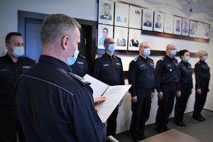 Naczelnik Wydziału Kadr podczas odczytania rozkazów personalnych, w tle policjanci biorący udział w uroczystości.