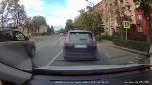 stopklatka z filmu zarejestrowanego wideorejestratorem samochodowym. Przed nagrywającym, przed przejściem dla pieszych stoi samochód. Z lewej strony nagrywającego przejeżdża drugi samochód.