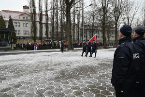 Przemarsz trzech policjantów wraz z Godłem Państwowym,  W tle widoczne rodziny policjantów , którzy uczestniczą w uroczystości ślubowania.