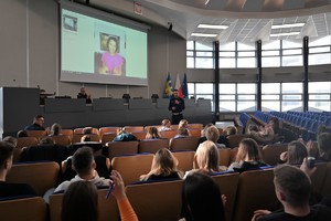 Zdjęcie. Widoczni uczestnicy briefingu oraz prowadzący, a także ambasadorka briefingu na ekranie podczas połączenia video
