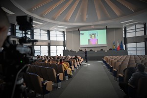 Zdjęcie. Widoczni uczestnicy briefingu oraz prowadzący, a także ambasadorka briefingu na ekranie podczas połączenia video