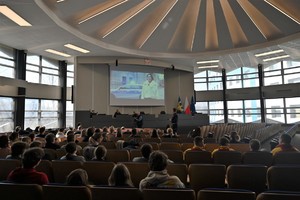 Zdjęcie. Widoczni uczestnicy briefingu oraz prowadzący, a także ambasadorka briefingu na ekranie podczas połączenia video