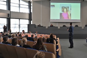 Zdjęcie. Widoczni uczestnicy briefingu oraz prowadzący, a także ambasadorka briefingu na ekranie podczas połączenia video