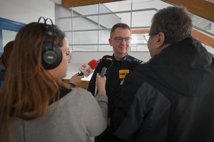 Zdjęcie. Policjant wypowiadający się przed mikrofonami dziennikarzy