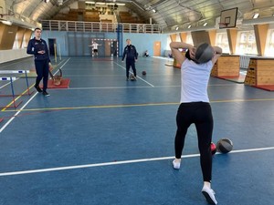 Na zdjęciu instruktorzy policyjni podczas nadzorowania przebiegu próbnego testu sprawnościowego. Na pierwszym planie widać uczestniczkę w trakcie wykonywania rzutu piłką lekarską