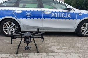 Na zdjęciu policyjny radiowóz oraz stojący obok niego dron.