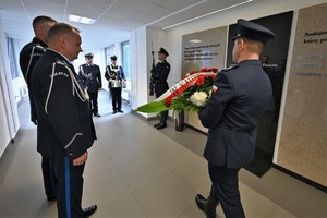 Zdjęcie. Umundurowani policjanci składają kwiaty przed tablicą