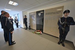Zdjęcie. Umundurowani policjanci składają kwiaty przed tablicą
