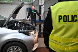 Kontroler sprawdza światła na stacji kontroli pojazdów. Z prawej strony stoi policjant.
