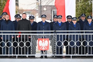 Komendant Krzystyniak stoi przy mikrofonie, a za jego plecami stoją oficjele.