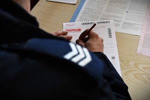Fragment policyjnego pagonu ze stopniem oraz ręce położone na formularzu.