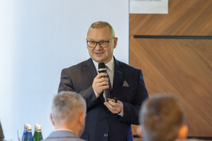 Grafika przedstawia prelegenta trzymającego mikrofon