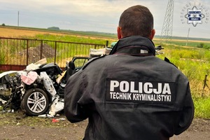 na zdjęciu policjant w kurtce z napisem policja technik kryminalistyki stojący przed rozbitym pojazdem