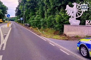 na zdjęciu fragment radiowozu i w oddali w rowie samochód wywrócony na bok