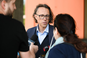Na zdjęciu widać trzy osoby. Dwie z nich trzymają mikrofon przy trzecim mężczyźnie.