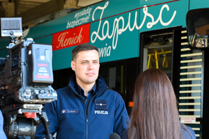 Na zdjęciu widać umundurowanego funkcjonariusza Policji, który udziela wywiadu dziennikarzowi.