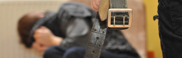 zdjęcie poglądowe obrazujące przemoc domową - kobieta zasłaniająca się, mężczyzny ręka z paskiem