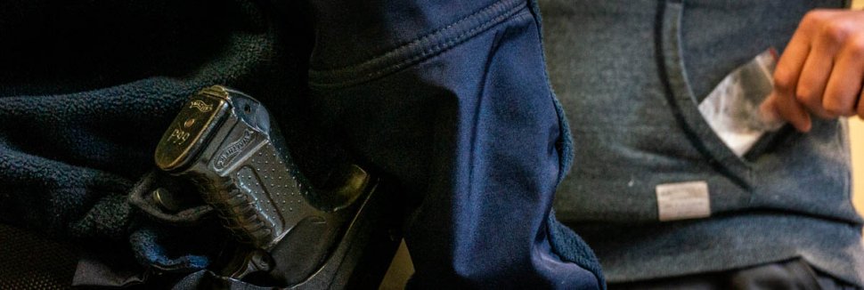 zdjęcie poglądowe - policjant, pistolet, w tle mężczyzna i woreczek z białym proszkiem wyjmowany z kieszeni bluzy