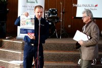 Policjant prezentuje plakat dotyczący oszustw na osobach starszych