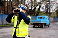 Policjant z lornetką na tle samochodu ciężarowego