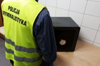 pomieszczenie - na blacie sejf obok stoi osoba w kamizelce z napisem policja kryminalistyka