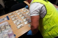 pomieszczenie, na stole rozłożone paczki z banknotami 200 złotowymi, osoba rozkładająca paczki w kamizelce z napisem policja