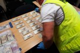 pomieszczenie, na stole rozłożone paczki z banknotami 200 złotowymi, osoba rozkładająca paczki w kamizelce z napisem policja