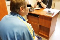 Zdjęcie - pokój, na pierwszym planie siedzi mężczyzna (sprawca) w kolorowej bluzie dresowej, w oddali biurko i policjant kryminalny prowadzący przesłuchanie