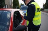 zdjęcie - policjant stojący przy czerwonym samochodzie legitymuje kierowcę w tle radiowóz policyjny - zdjęcie archiwalne