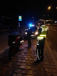 zdjęcie przedstawia policjanta drogówki, motocyklistę z motorem i w tle radiowóz