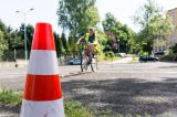 zdjęcie przedstawia - biało pomarańczowy pachołek a w tle rowerzystkę w trakcie egzaminu