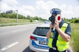 zdjęcie przedstawia policjanta drogówki z radarowym miernikiem prędkości w trakcie dokonywania pomiaru