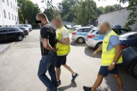 zdjęcie przedstawia, plac parkingowy, stojące w tle radiowozy - dwóch policjantów i zatrzymany