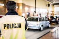 zdjęcie - wnętrze stacji diagnostycznej, na pierwszym planie policjant drogówki tyłem w tle samochody